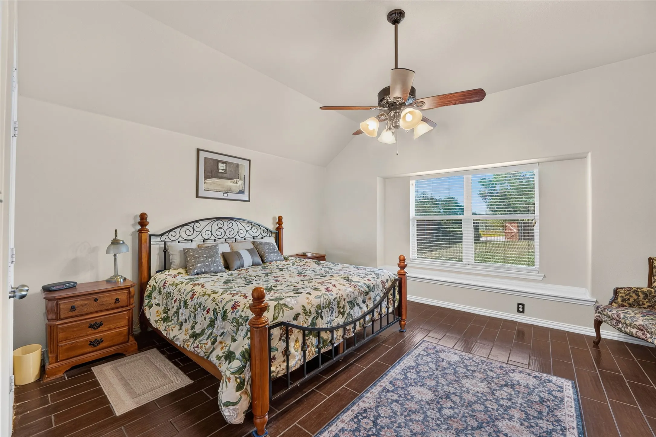 Spacious primary bedroom featuring vaulted ceilings with fan, abundant natural light, and a cozy window seat overlooking the backyard.