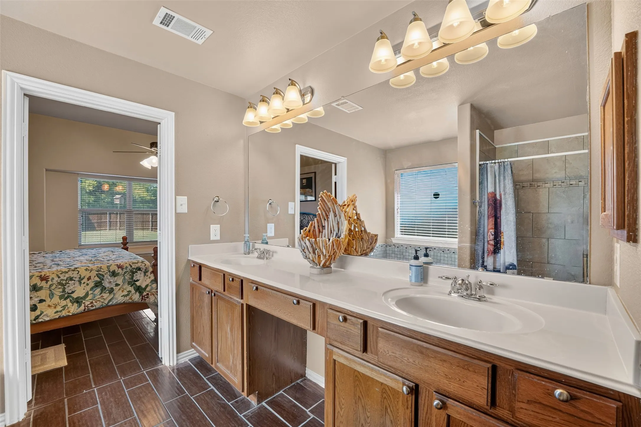 Dual-sink vanity with full-width vanity mirror, multi-light fixtures, and tiled shower and bath surround.