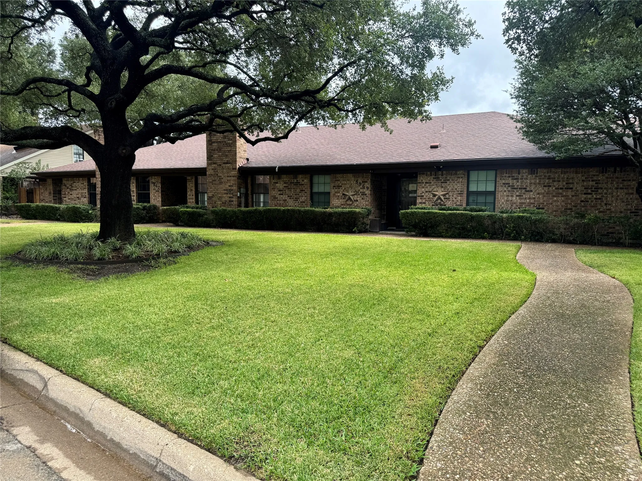 Single-story brick exterior featuring a prominent chimney, concrete walkway, and mature landscape trees