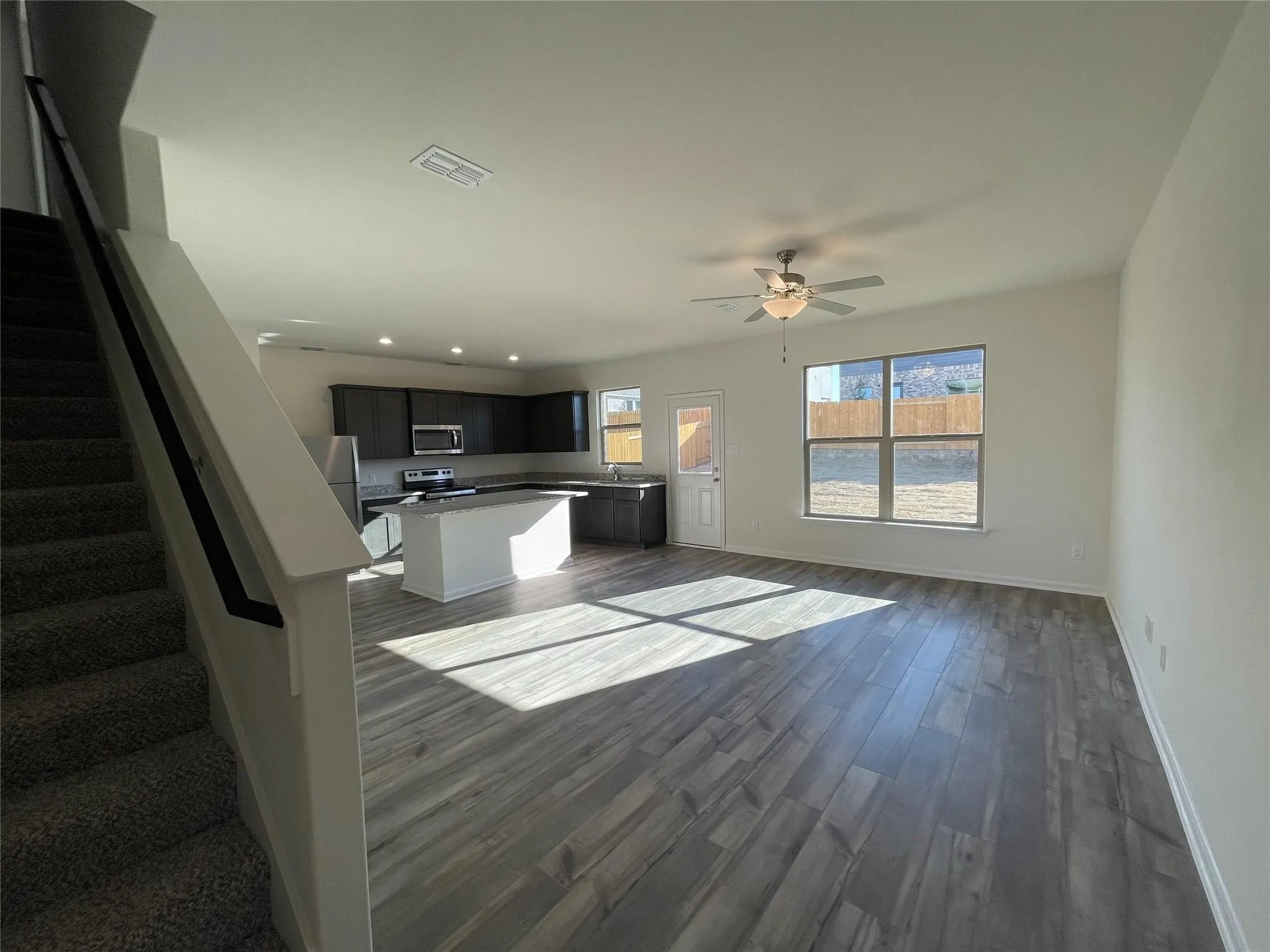 Open floor plan featuring wood-finish flooring, a kitchen island, dark cabinetry, and a ceiling fan