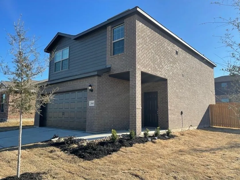 Two-story exterior featuring a brick facade with horizontal siding accents, a concrete driveway, a covered entry, and a multi-panel garage door