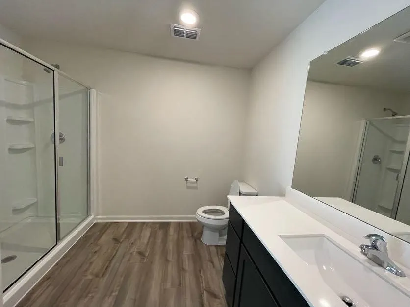 Bathroom featuring a glass-enclosed shower, wood-finish flooring, dark cabinetry with a white countertop, and a full-width wall mirror