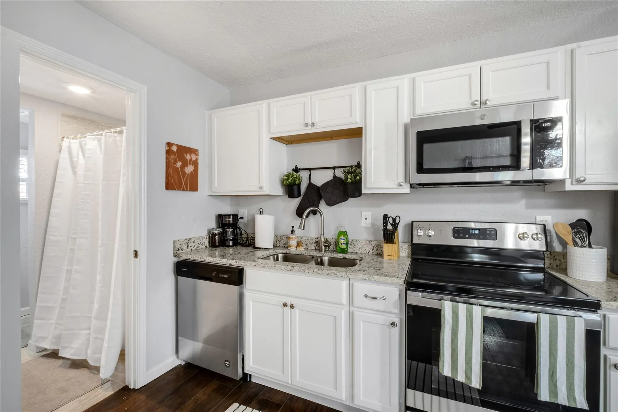 Kitchen featuring white shaker-style cabinetry, stone-finish countertops, stainless steel appliances, and wood-finish flooring