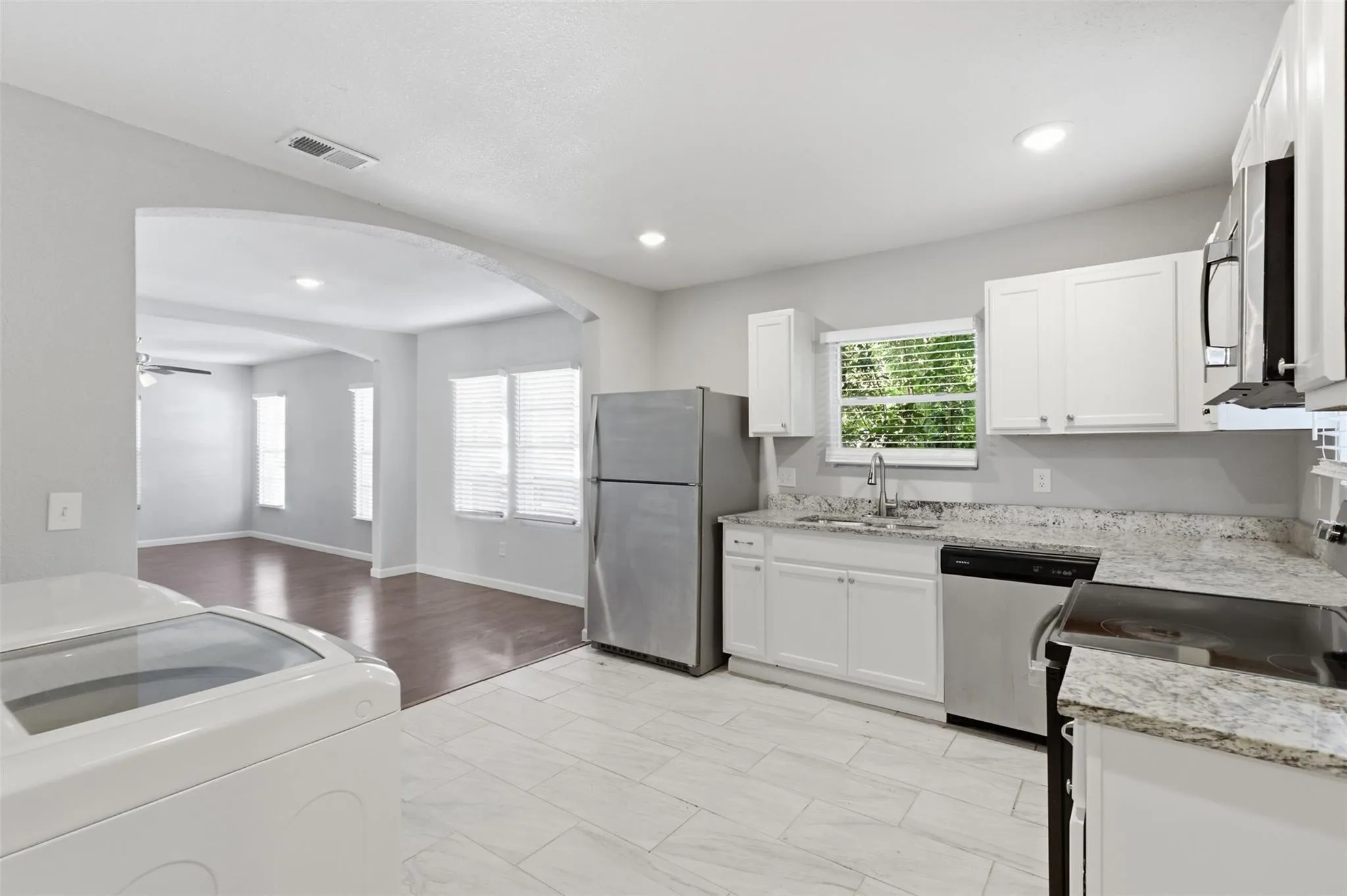 Kitchen featuring white cabinetry, stone-finish countertops, stainless steel appliances, and large-format tile flooring, highlighted by an arched architectural opening