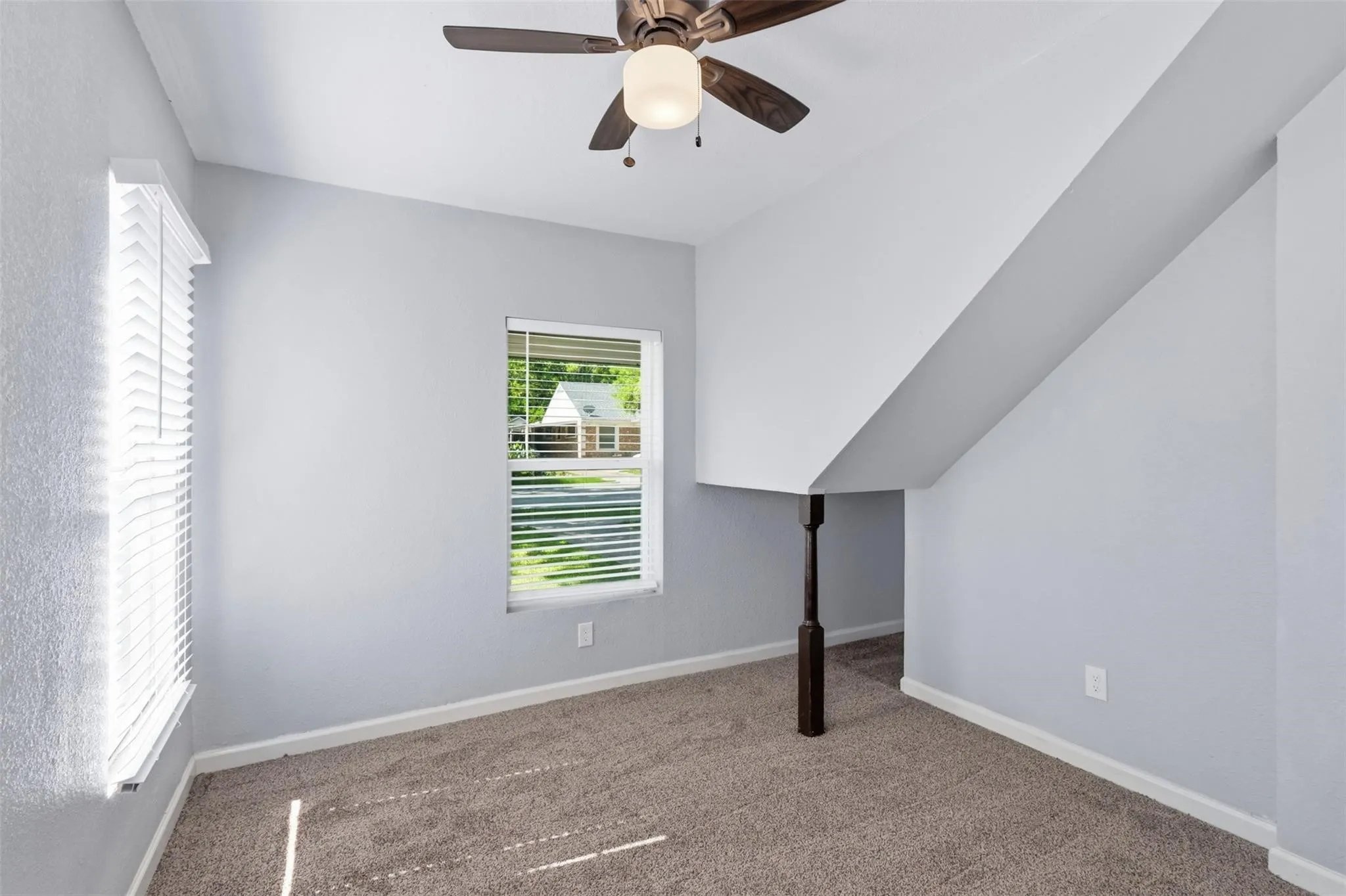 Neutral wall coloring with carpeted flooring, a ceiling fan with integrated lighting, and a dark-toned decorative support column