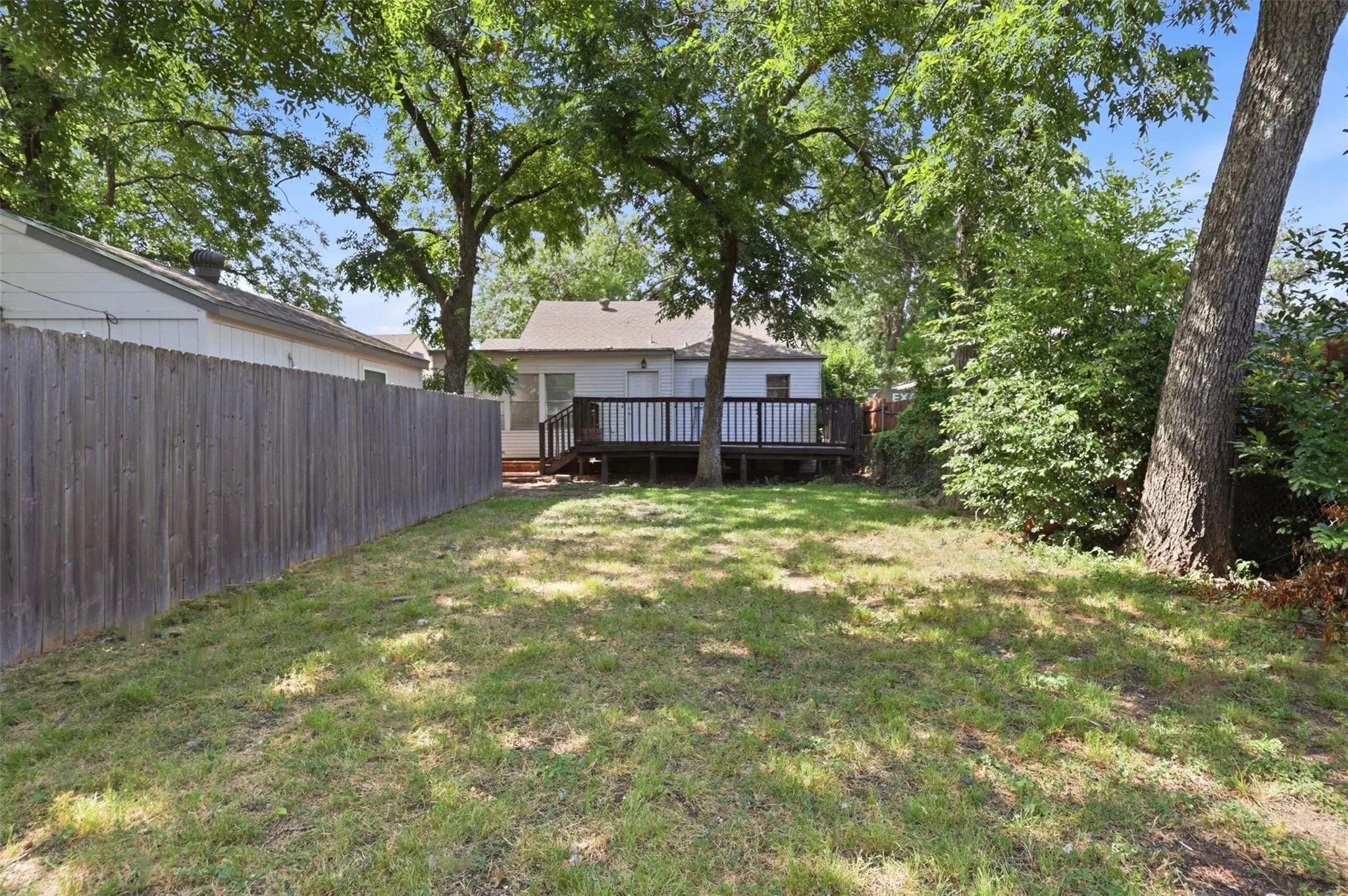Backyard featuring a wood deck, vertical board fencing, and mature trees