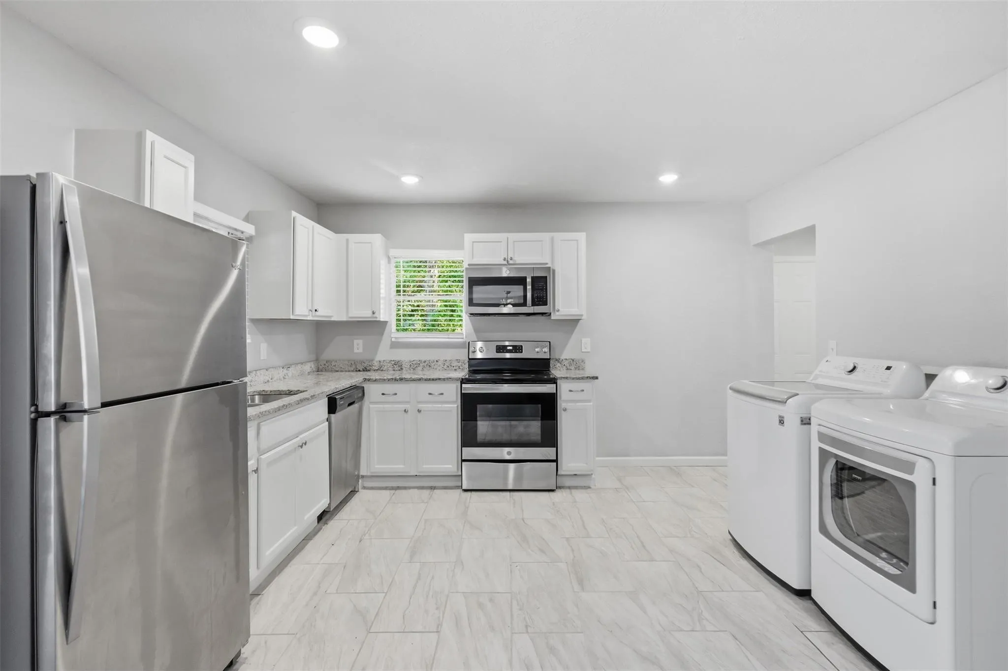 Kitchen featuring white shaker-style cabinetry, stone-finish countertops, stainless steel appliances, and tile flooring