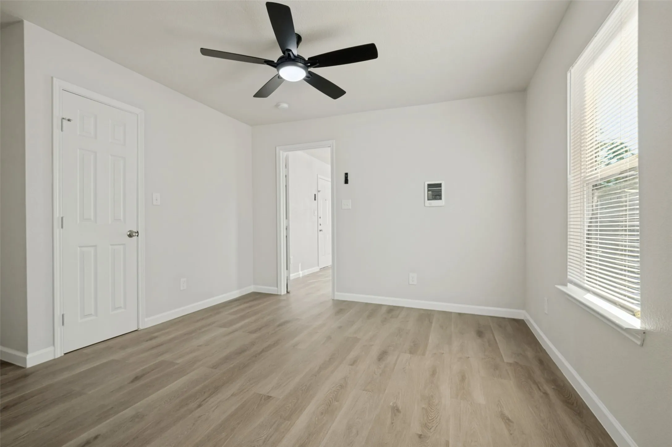 Neutral interior space featuring wood-finish flooring, a ceiling fan with integrated lighting, and a window with horizontal blinds