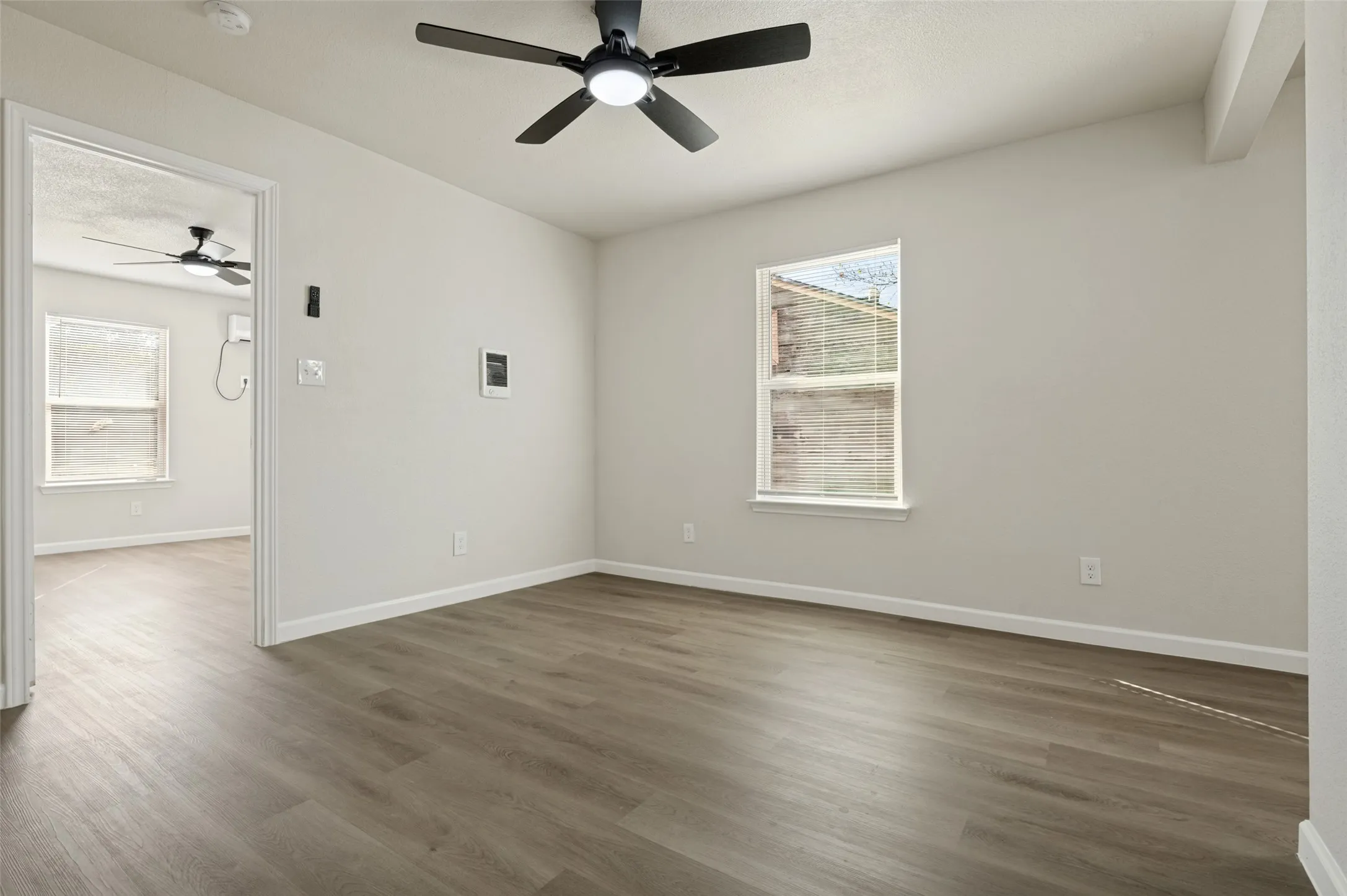 Neutral wall palette featuring wood-finish flooring, recessed windows, and a matte black ceiling fan with integrated lighting