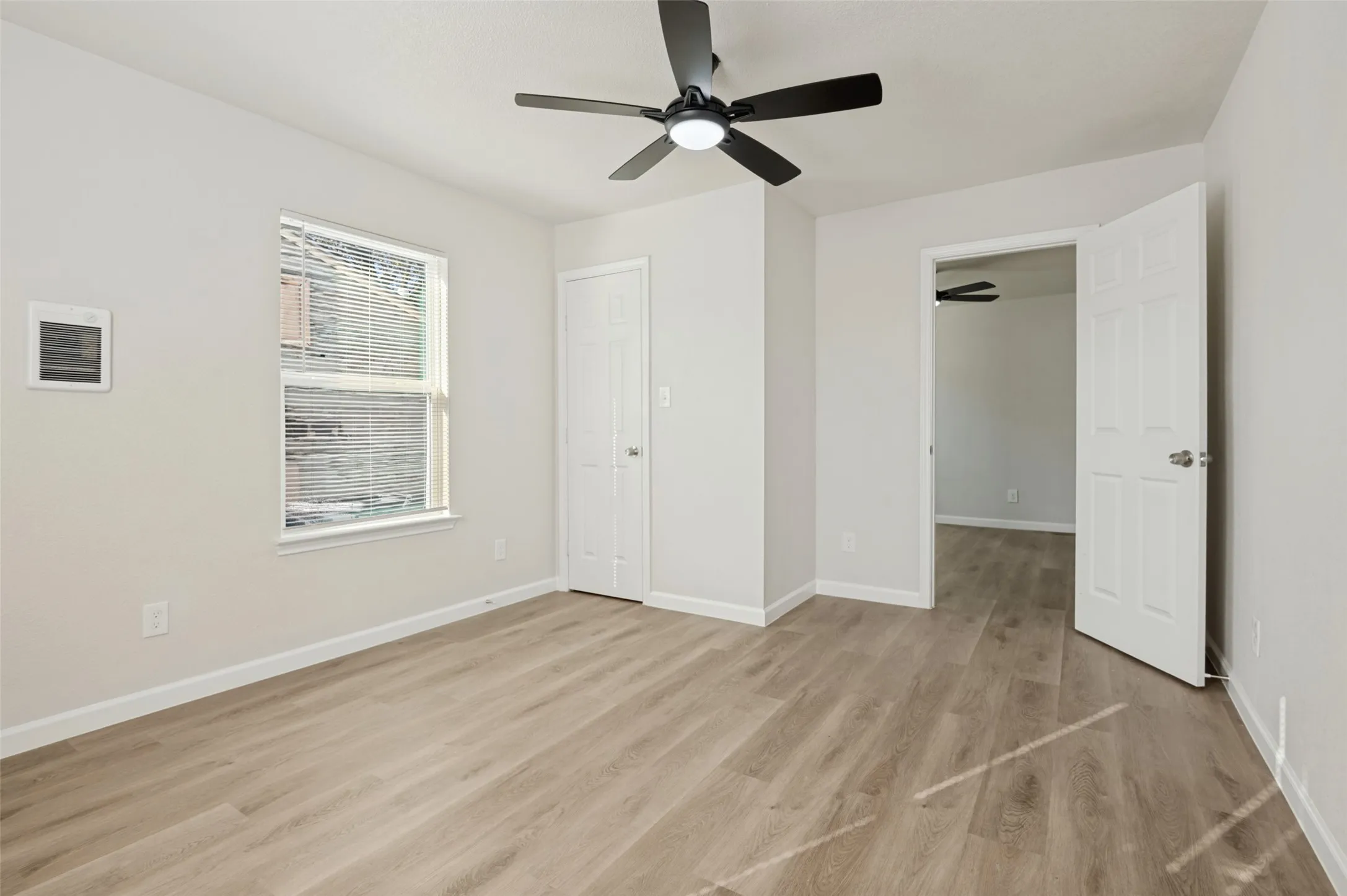 Neutral-toned room featuring wood-finish flooring, a ceiling fan with integrated lighting, and a six-panel door