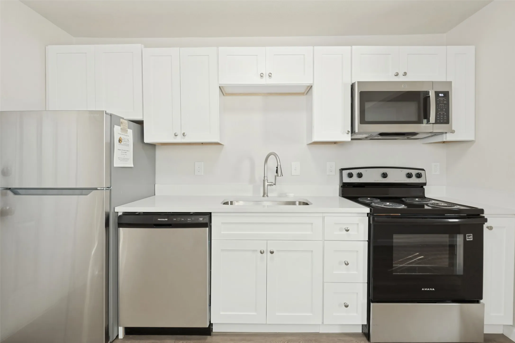 Kitchen featuring white shaker-style cabinetry, solid-surface countertops, stainless steel appliances, and a gooseneck faucet