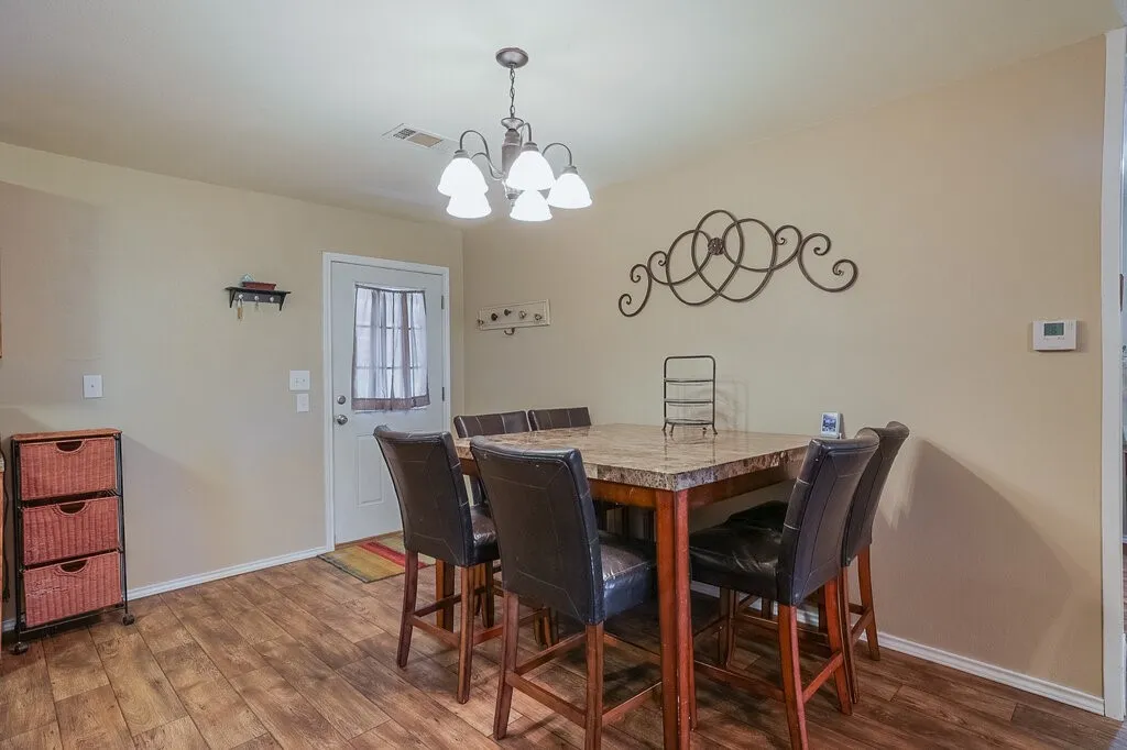 Dining area featuring wood-finish flooring, a five-arm multi-bulb chandelier, and a single-entry door with a central glass pane
