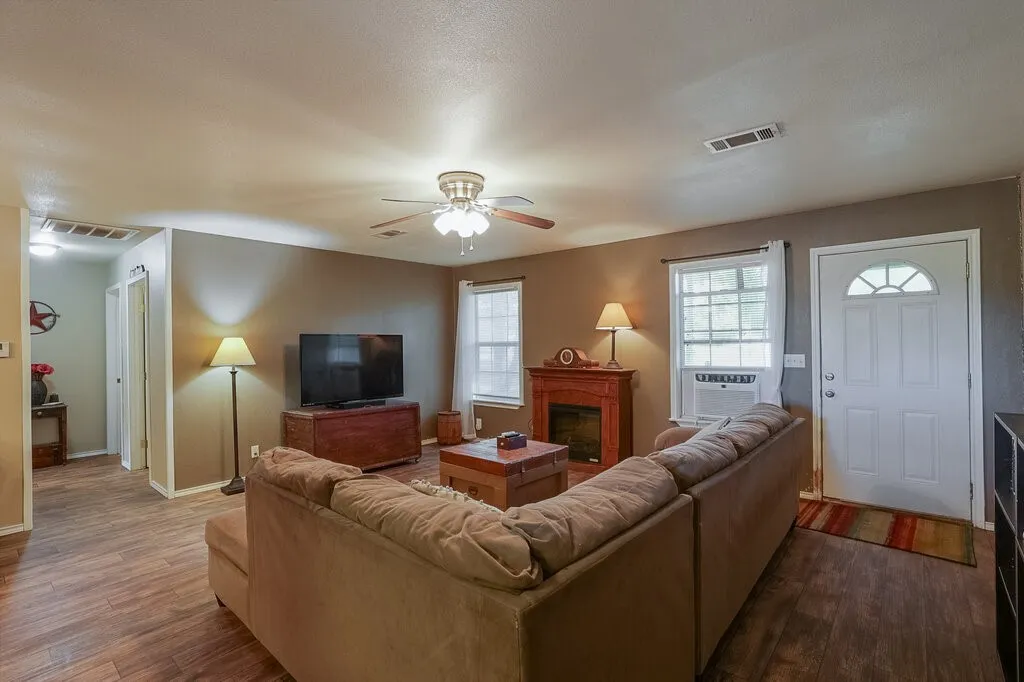 Living area featuring wood-finish flooring, a ceiling fan with integrated lighting, a fireplace with a wood-finish mantel, and a multi-panel exterior door with a transom window