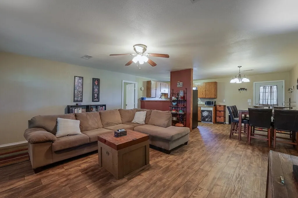 Open-concept interior featuring wood-finish flooring, a central ceiling fan with integrated lighting, a multi-pendant dining fixture, and kitchen cabinetry