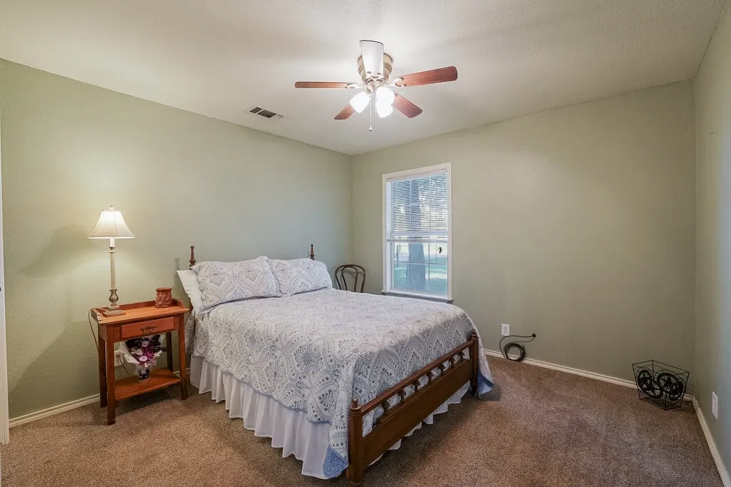 Neutral-toned interior walls, carpeted flooring, single-pane window, and a multi-blade ceiling fan with integrated light fixture