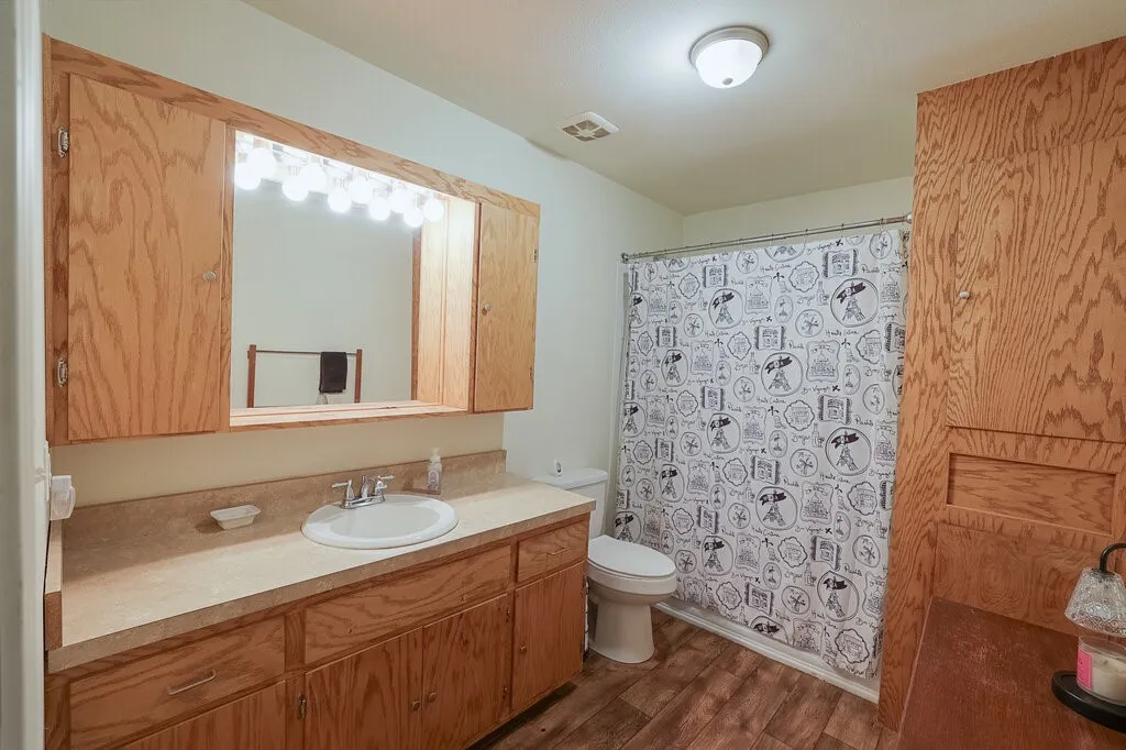 Bathroom featuring a wood-finish vanity with a drop-in sink, expansive built-in cabinetry, wood-finish flooring, and a shower-tub combination