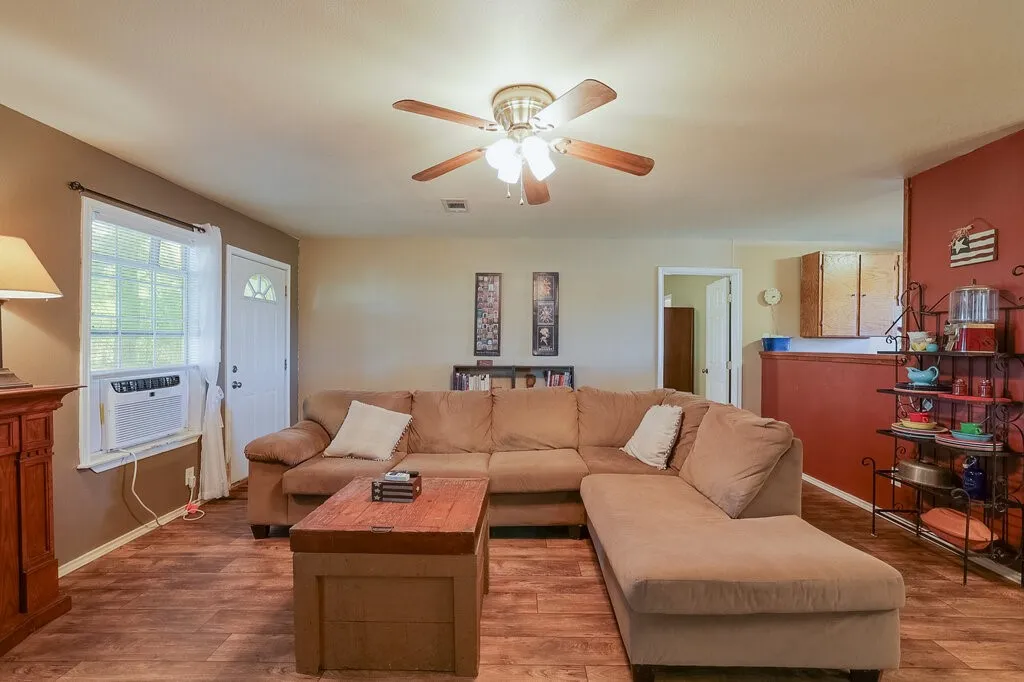 Wood-finish flooring, central ceiling fan with integrated lighting, and a half-wall partition