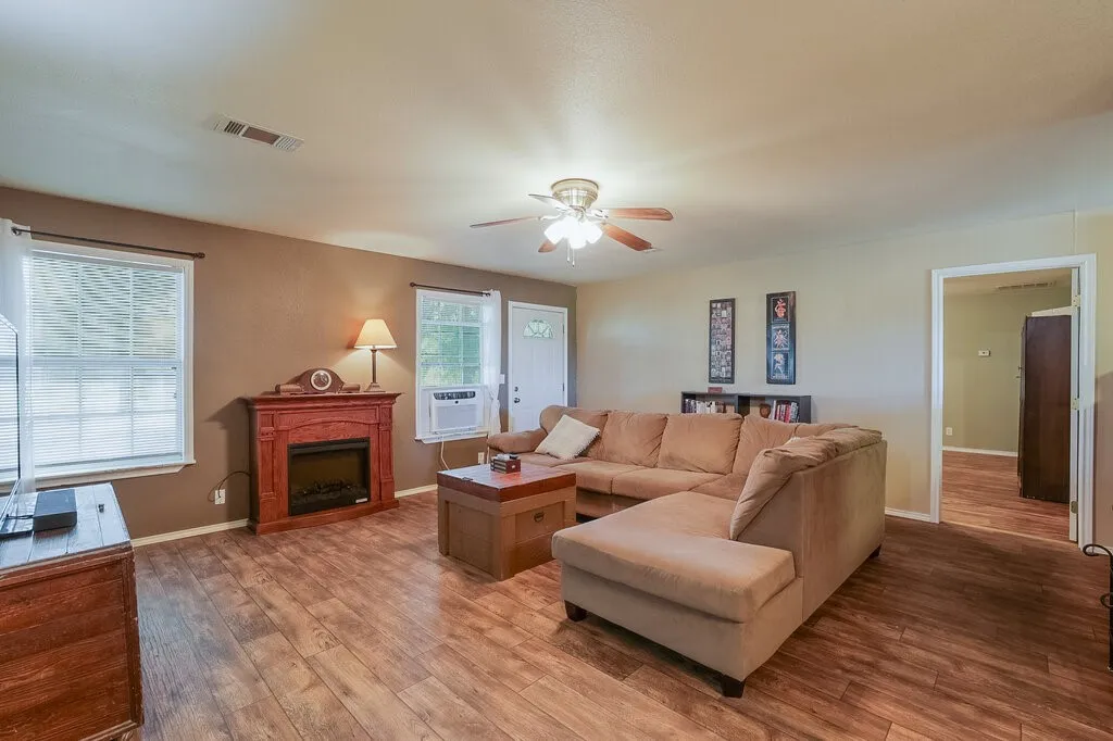 Living area featuring wood-finish flooring, a built-in decorative fireplace, and a ceiling fan with integrated lighting