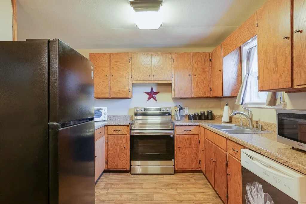 Kitchen featuring wood-finish cabinetry, stone-texture countertops, wood-finish flooring, stainless steel range, and stainless steel dual-basin sink with gooseneck faucet