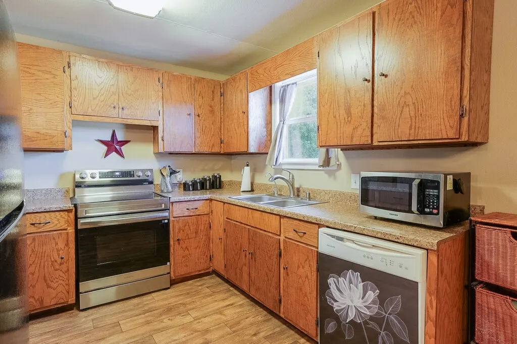 Kitchen featuring wood cabinetry, stone-finish countertops, wood-finish flooring, stainless steel range, and double-basin sink with faucet
