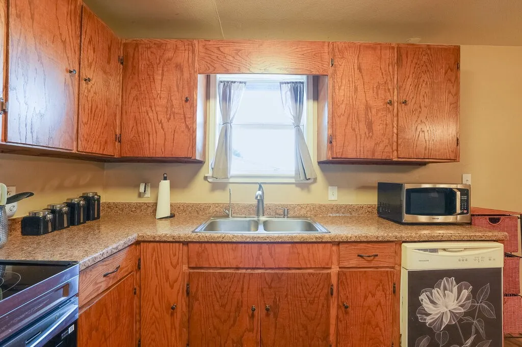 Kitchen featuring wood-finish cabinetry, stone-pattern laminate countertops, dual-basin stainless steel sink with pull-down faucet, and built-in dishwasher