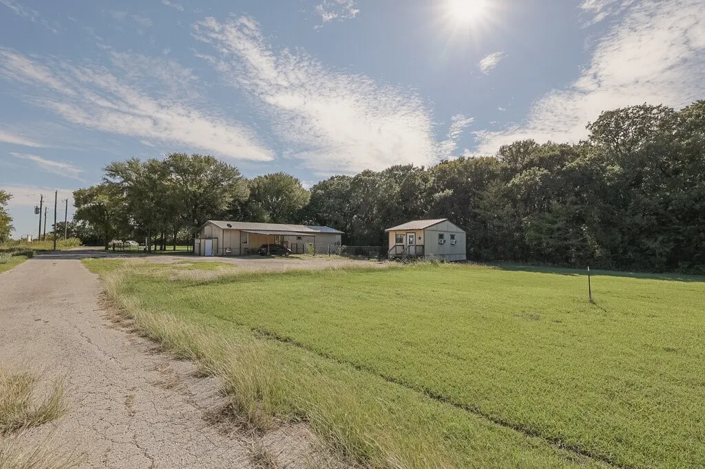 Expansive acreage featuring a paved approach, open green space, a detached garage with a covered carport, and a separate structure with wood-tone siding