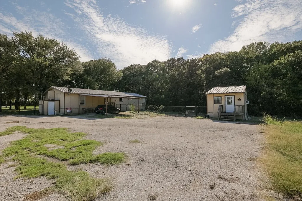 Exterior structures featuring metal roofing, a covered carport, and a chain-link fenced perimeter situated on a gravel lot