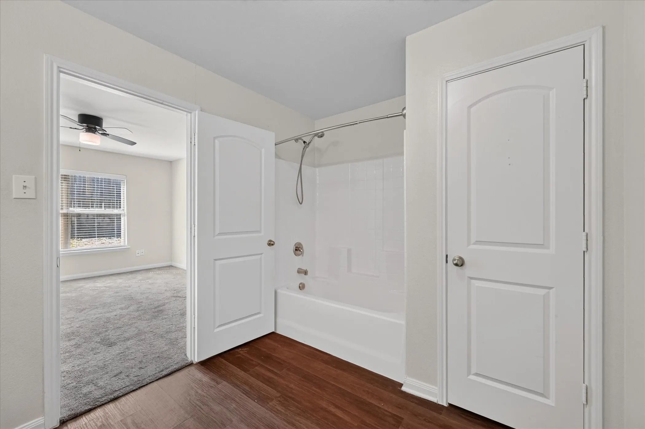Bathroom featuring a tub-shower combination with a white surround, wood-finish flooring, two-panel interior doors, and a brushed nickel shower faucet