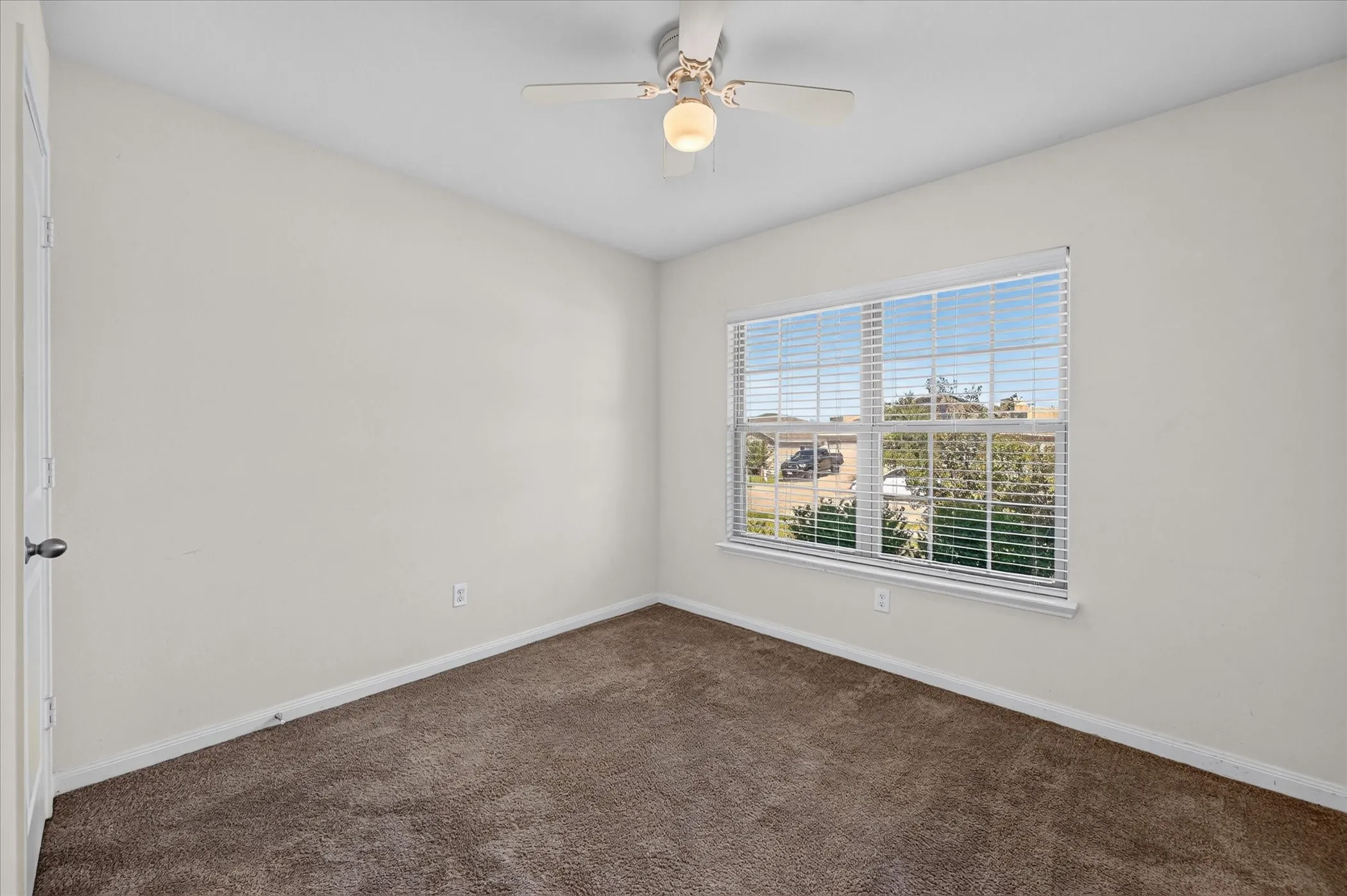Neutral-toned interior featuring wall-to-wall carpeting, a multi-pane window with installed blinds, and a central ceiling fan with an integrated light fixture