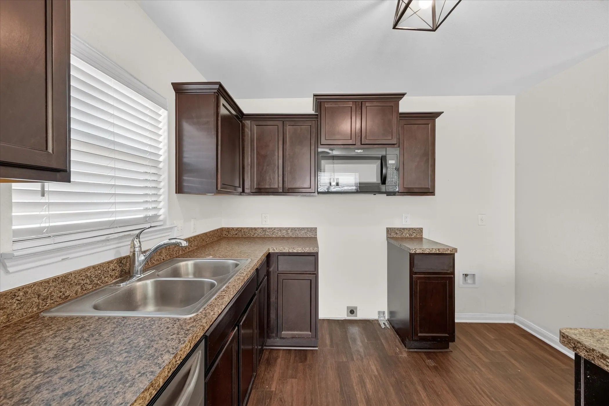 Dark-finish cabinetry paired with speckled laminate countertops, dual-basin stainless steel sink, built-in microwave, and wood-finish flooring