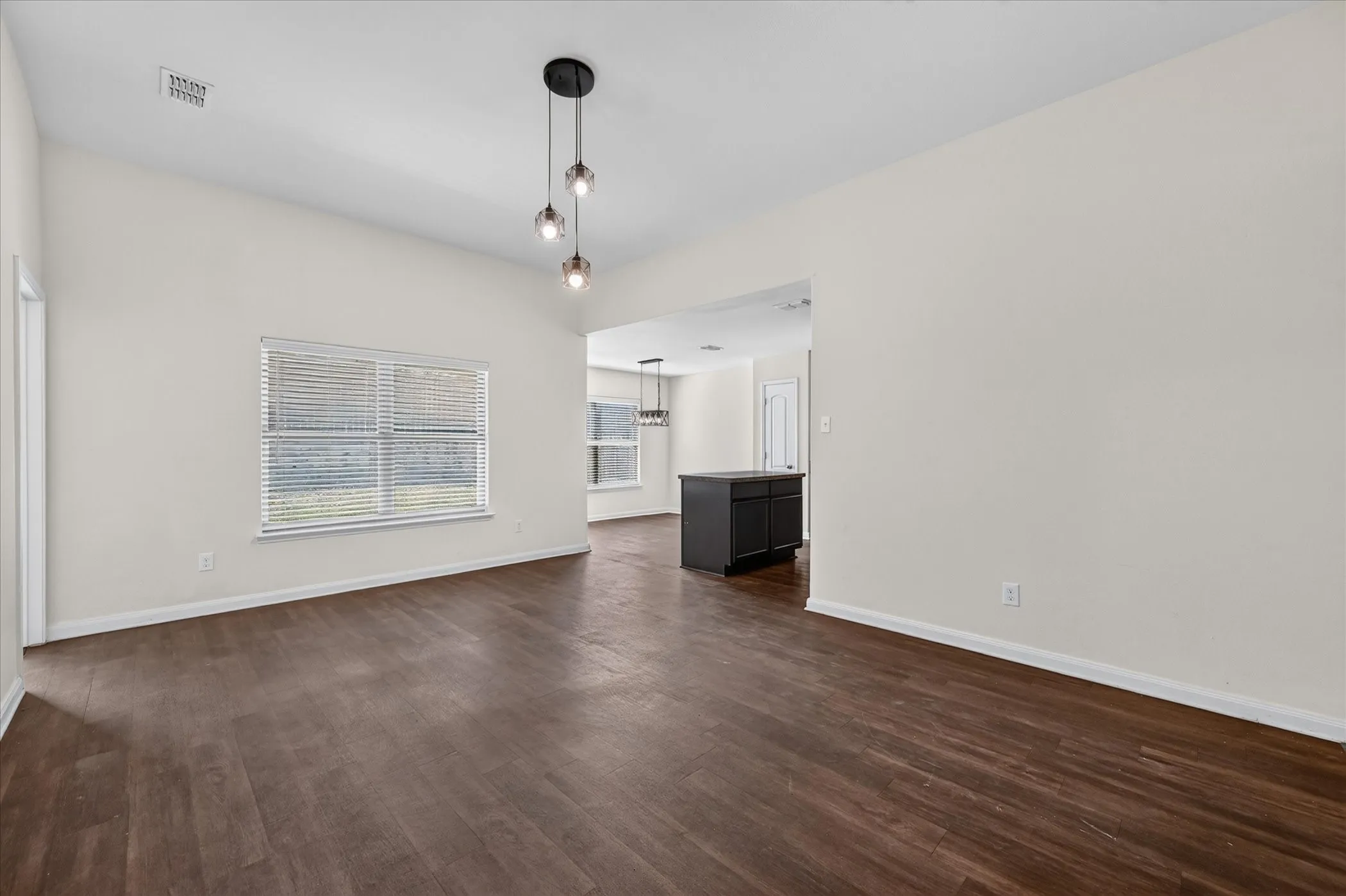 Interior space featuring high ceilings, wood-finish flooring, a multi-light pendant fixture, and large windows with horizontal blinds