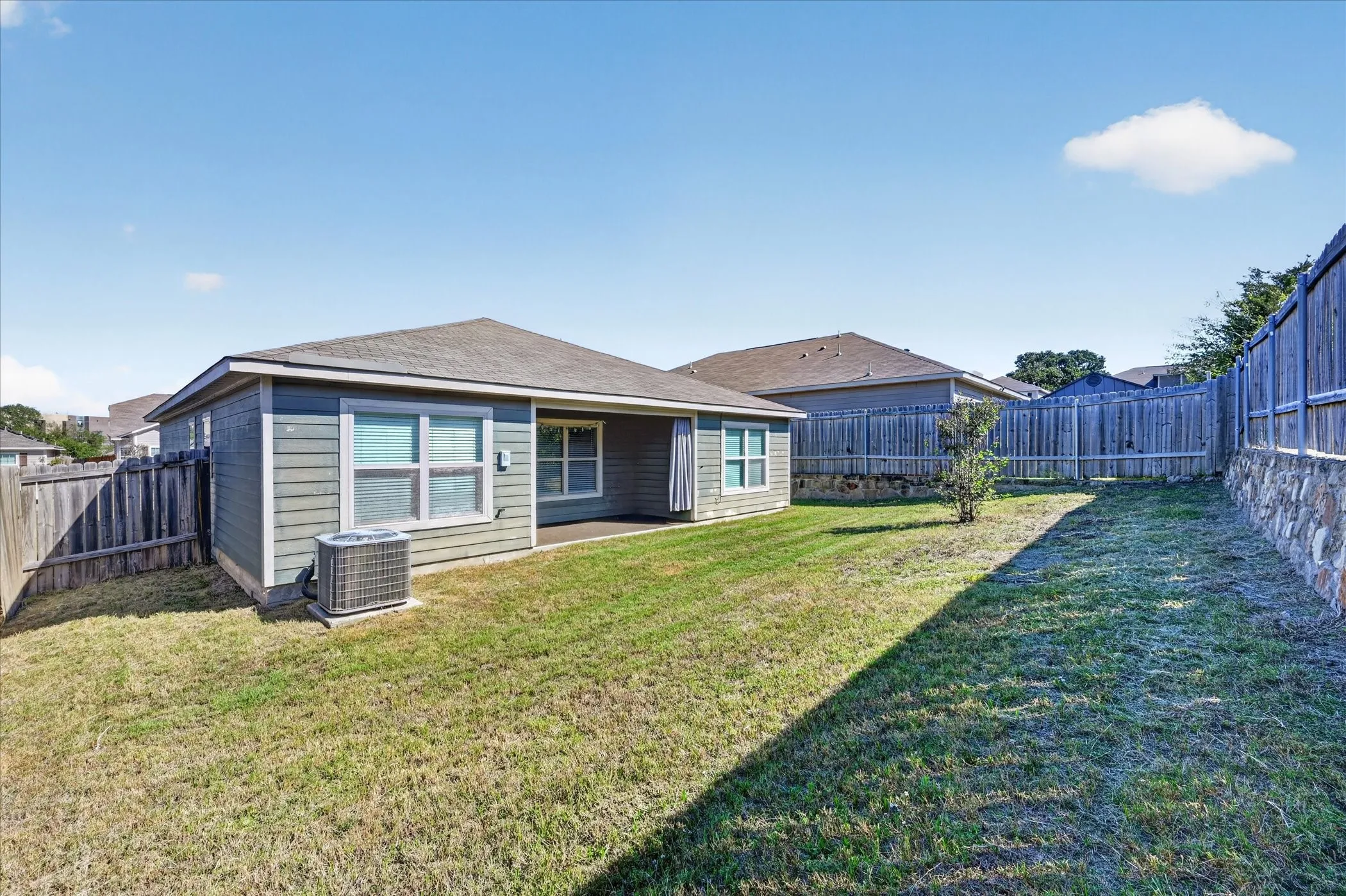 Rear exterior featuring horizontal lap siding, a covered patio, and a tiered retaining wall with stone-finish accents enclosed by wood fencing