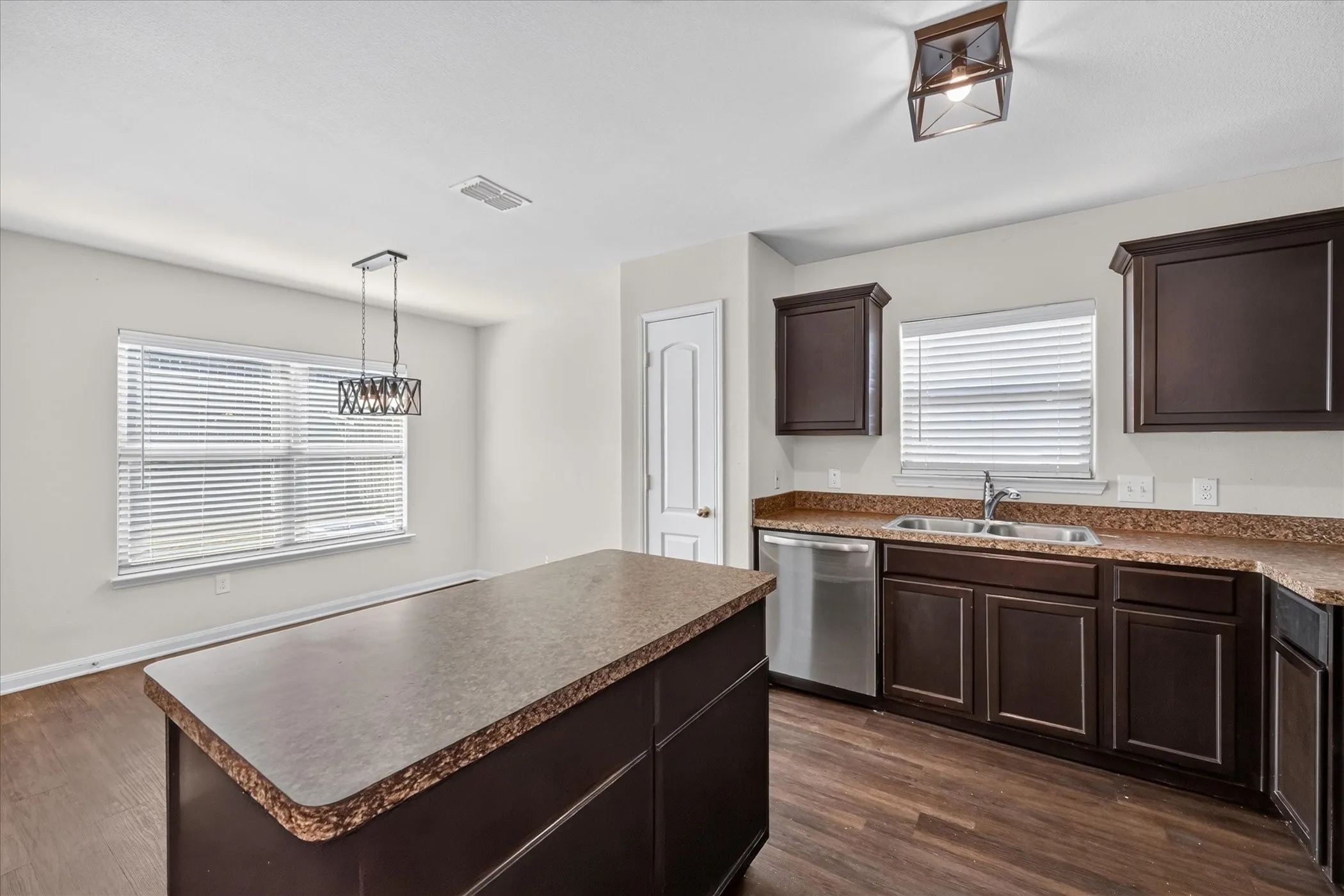 Kitchen featuring dark cabinetry, expansive countertops, a central island, stainless steel dishwasher, and wood-finish flooring