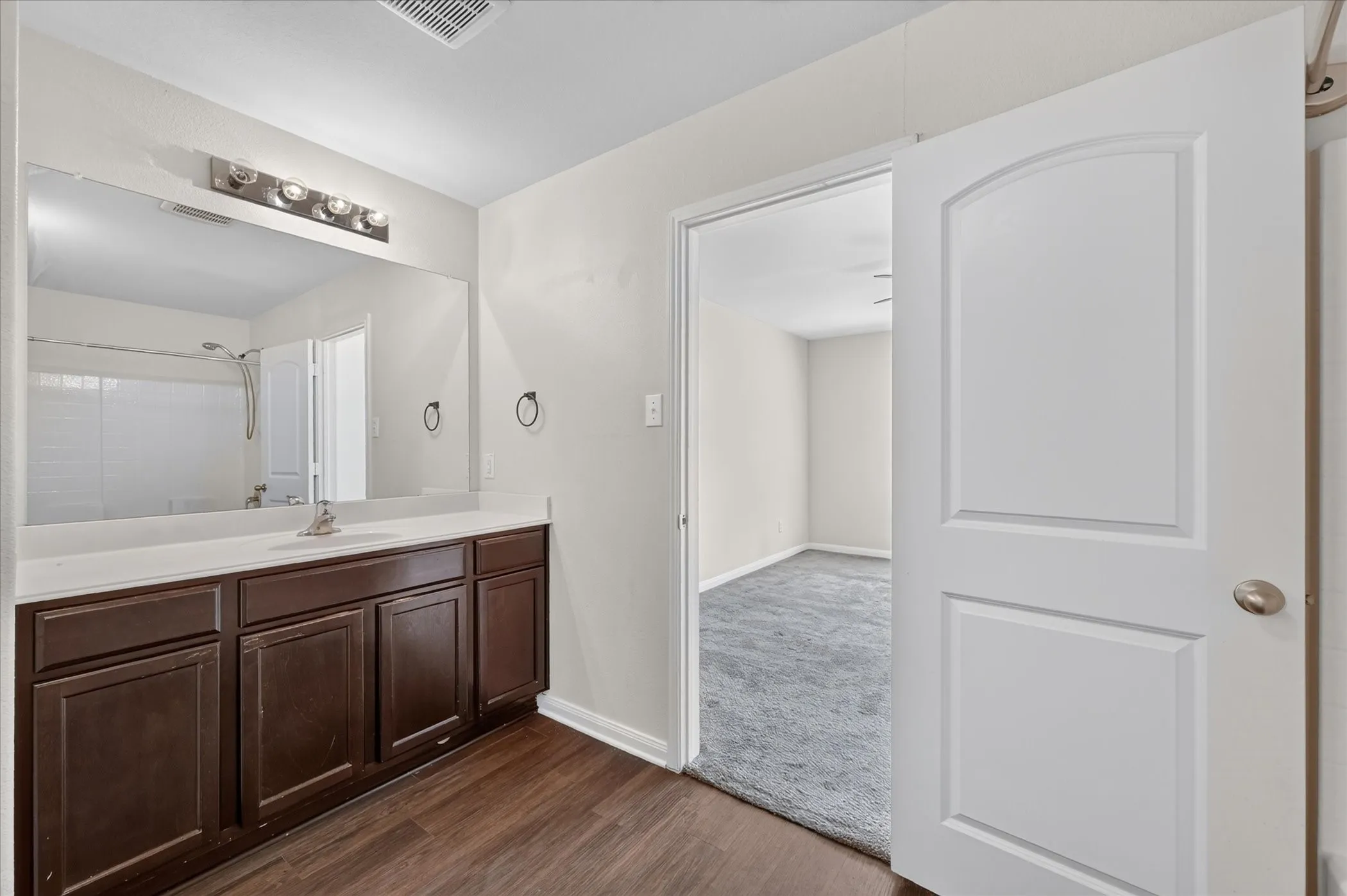 Bathroom featuring a dark wood-finish vanity, solid-surface countertop, full-width vanity mirror, and wood-finish flooring