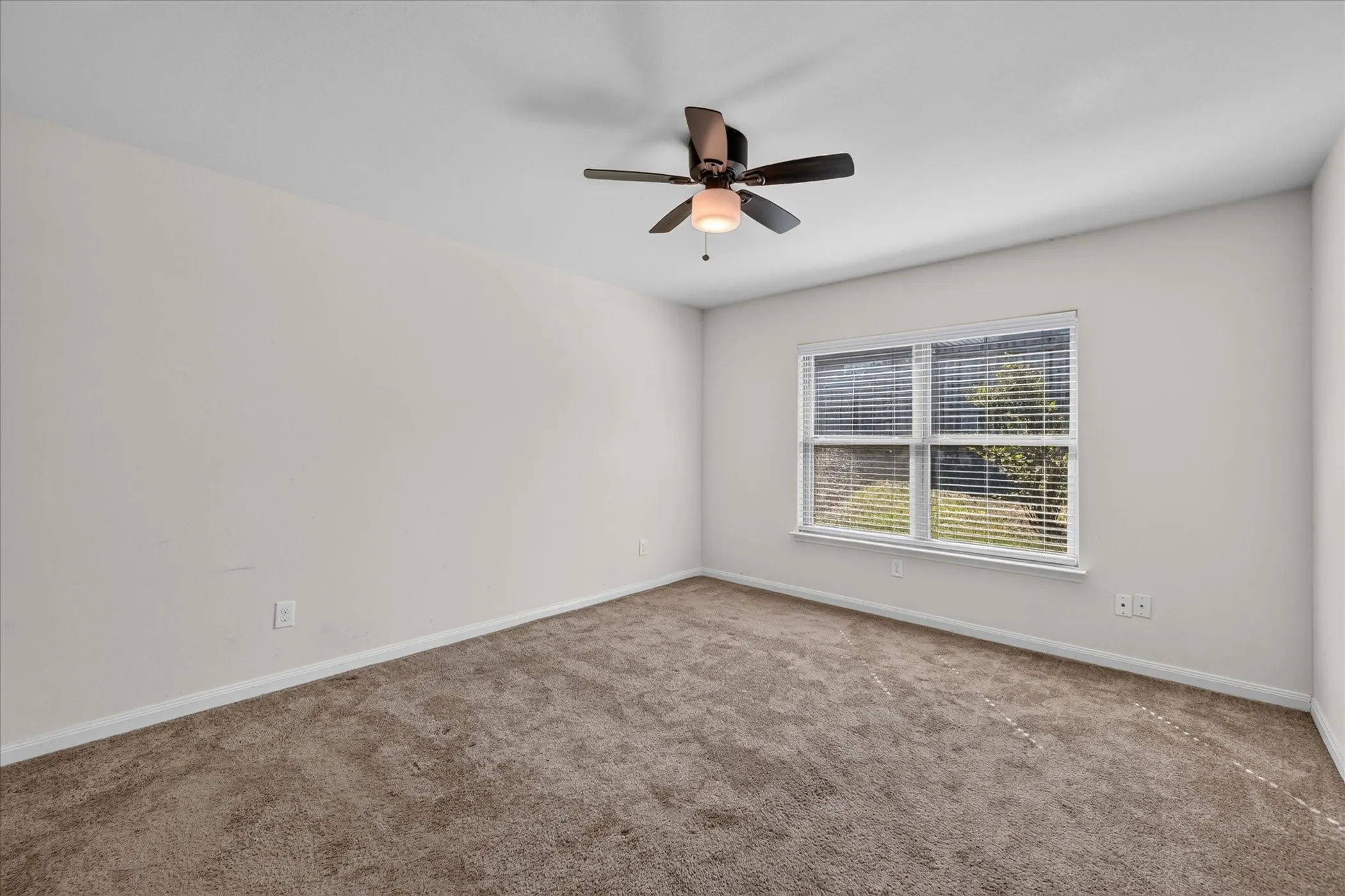 Neutral-toned wall interior featuring plush wall-to-wall carpeting, a multi-blade ceiling fan with an integrated light fixture, and a dual-pane window