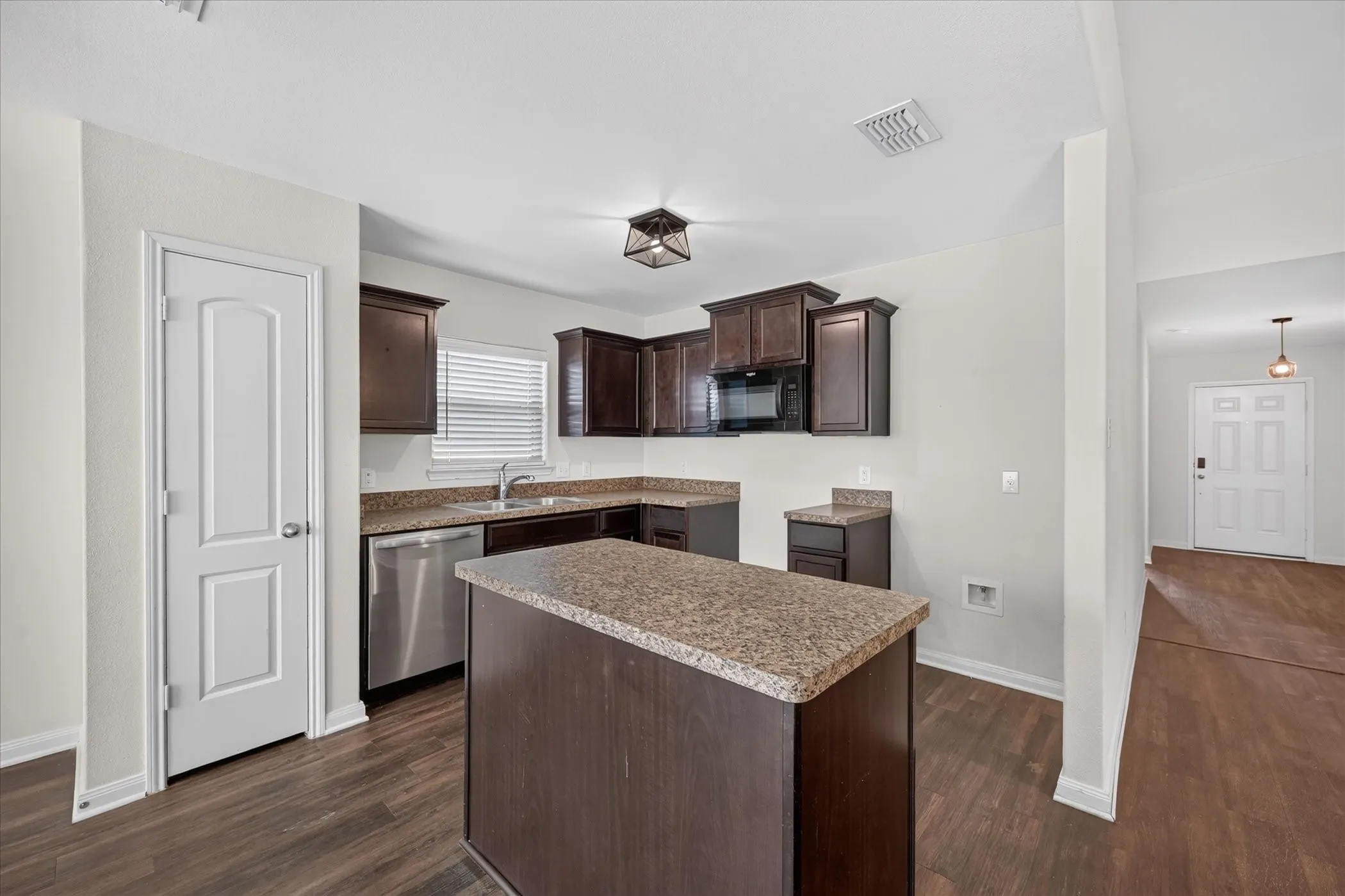 Kitchen featuring dark wood-finish cabinetry, a center island, stone-finish countertops, stainless steel appliances, and wood-finish flooring
