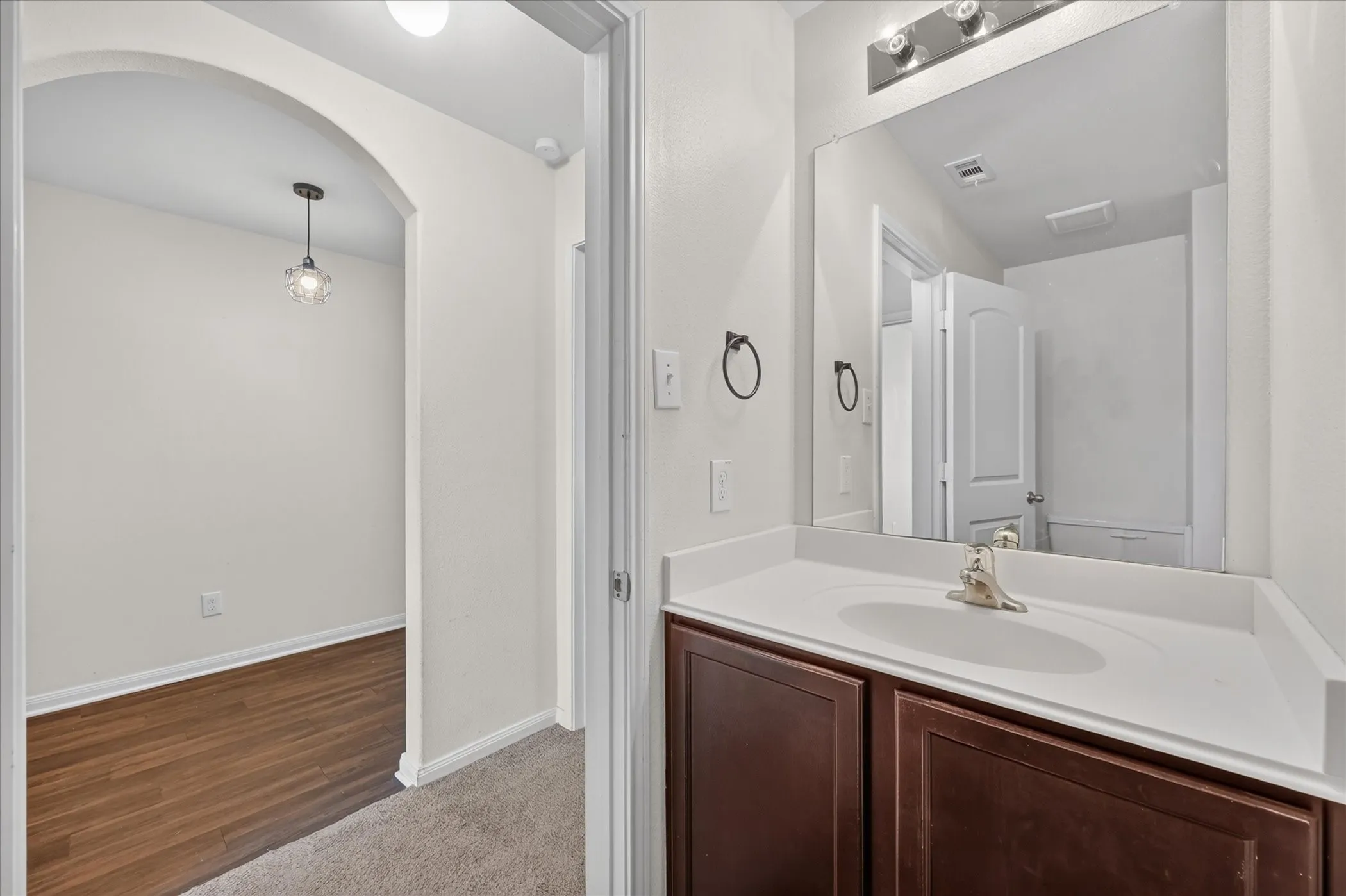 Vanity featuring a dark-finish wood cabinet, integrated sink, and wall-mounted light fixture, paired with a full-width mirror and an arched entryway