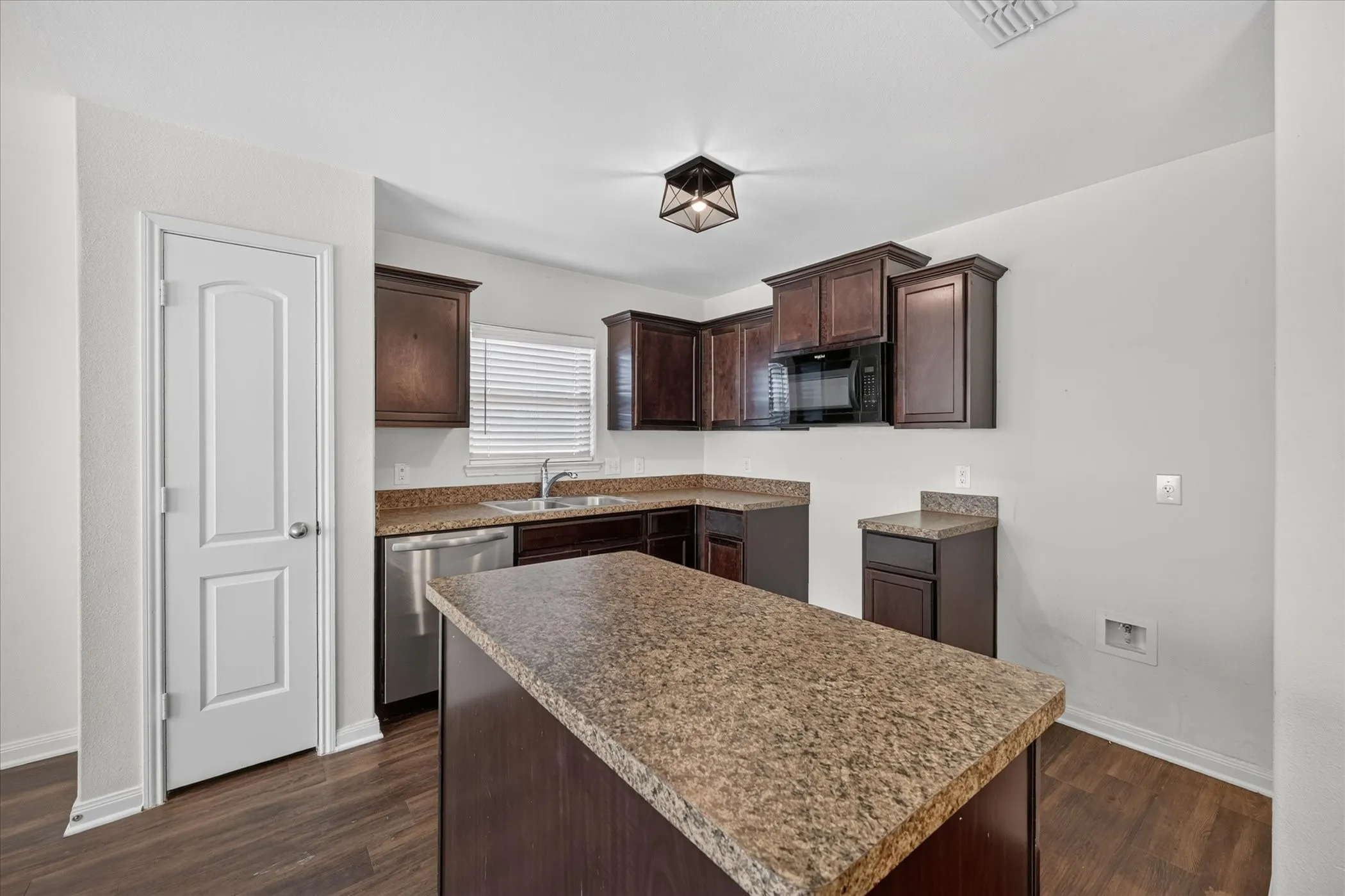 Kitchen featuring dark-toned cabinetry, a center island with countertop, stainless steel dishwasher, integrated microwave, and wood-finish flooring