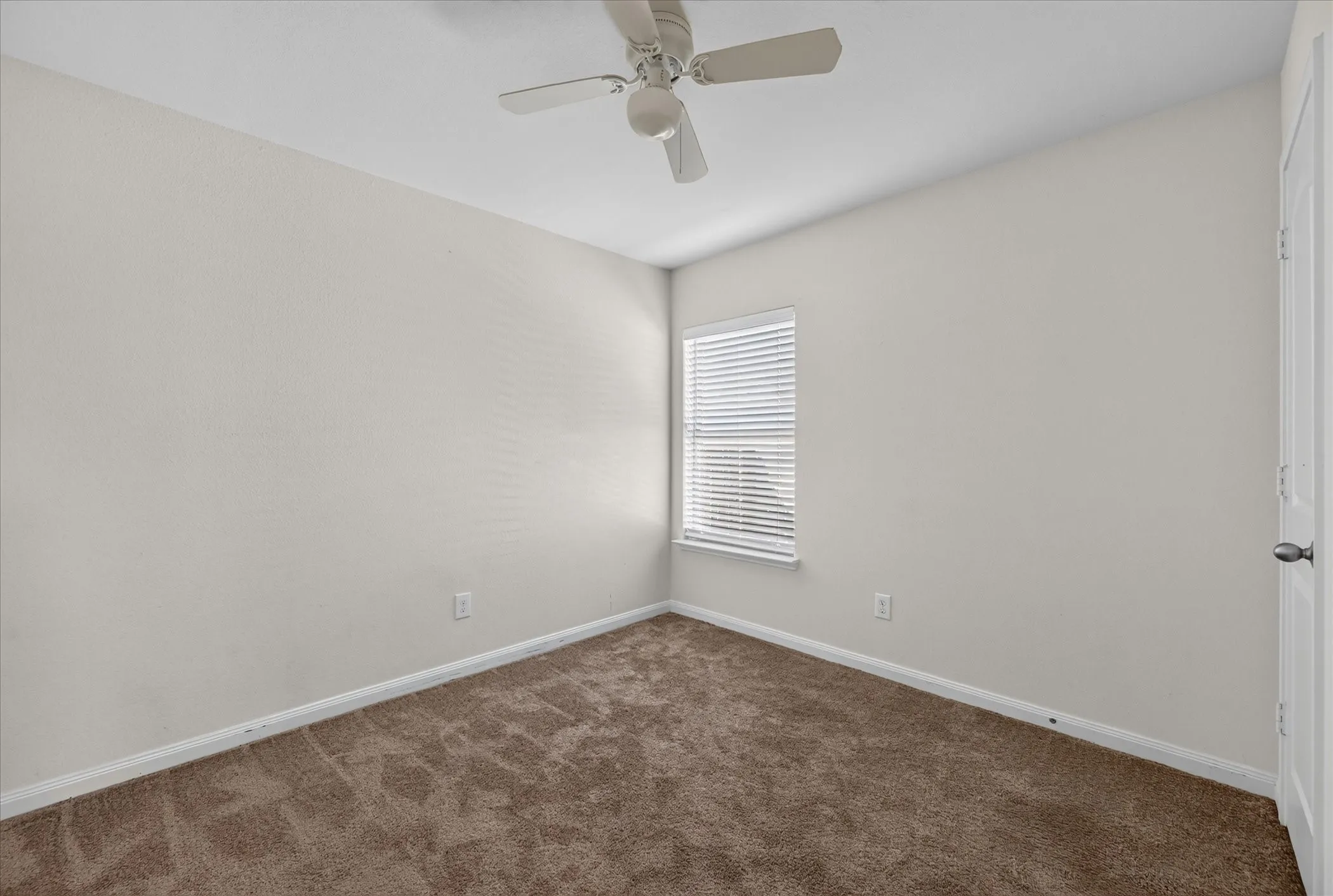 Neutral-toned interior space featuring neutral wall-to-wall carpeting, a multi-blade ceiling fan, and a single window with horizontal blinds