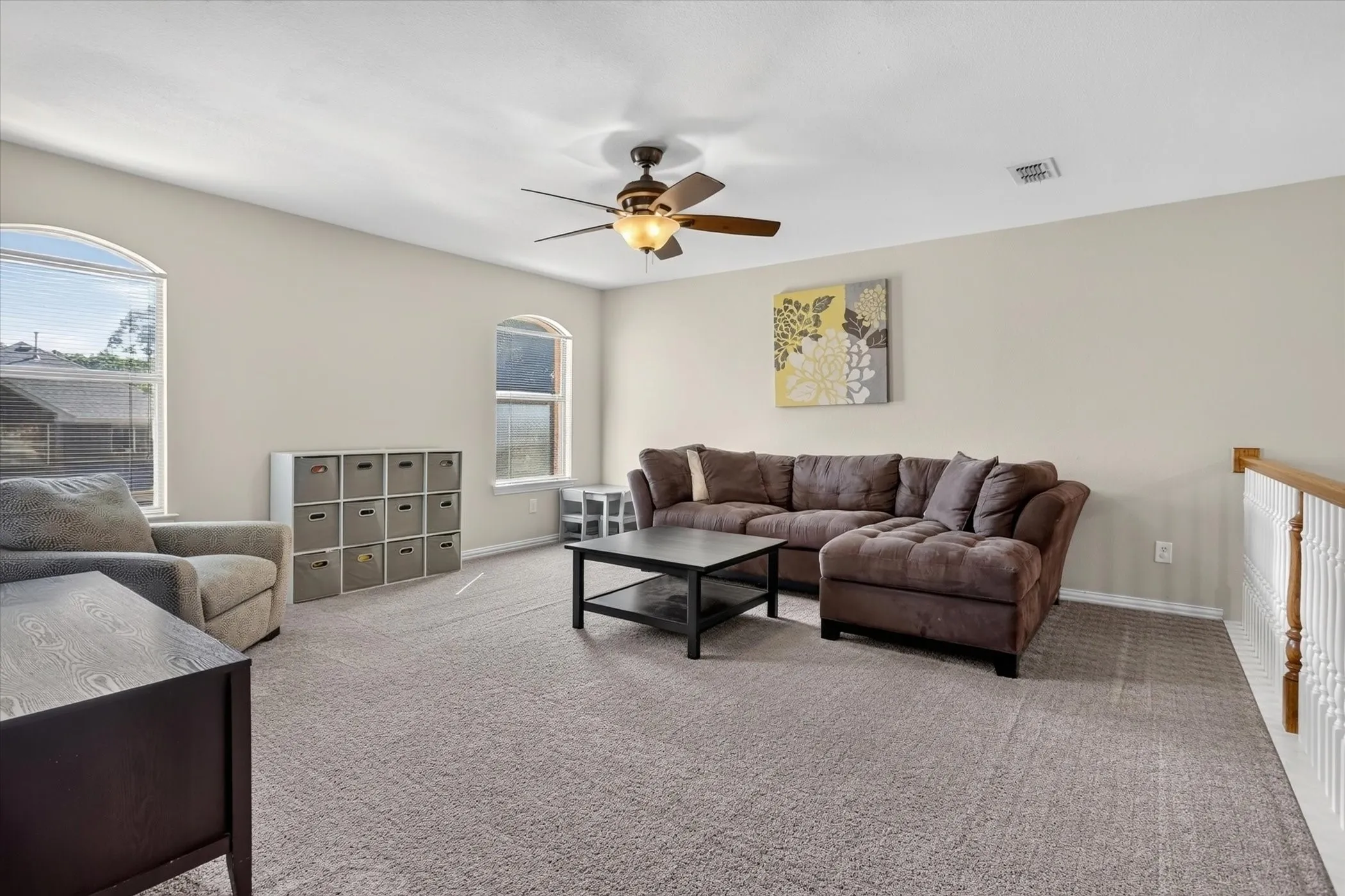 Neutral-toned interior featuring wall-to-wall carpeting, dual arched windows, a centrally mounted ceiling fan with integrated lighting, and a white wooden banister