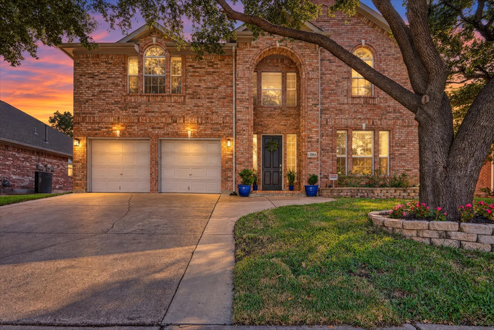 Two-story brick exterior featuring an arched entryway, double-car garage, and tiered stone landscape curbing