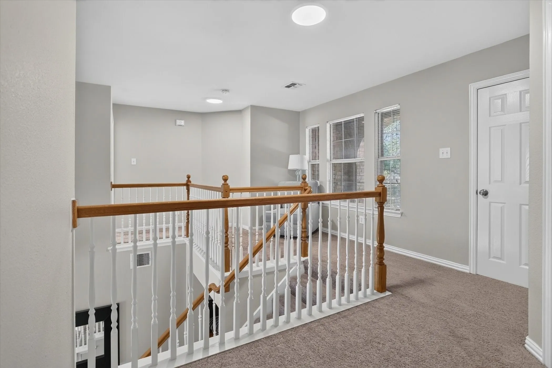 Landing area featuring a wooden handrail, white balusters, neutral carpeted flooring, and multiple window openings