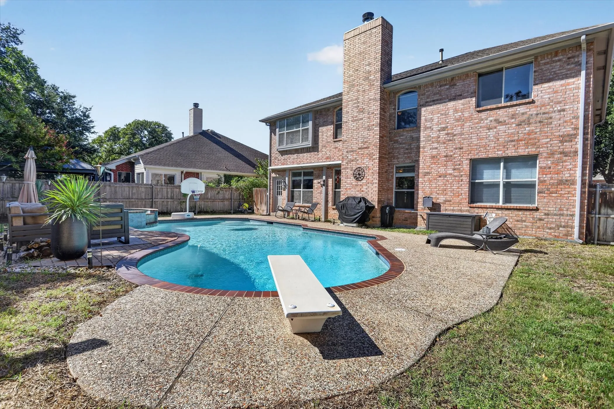 Brick exterior rear elevation featuring a swimming pool with a diving board, aggregate concrete patio, and a tall masonry chimney