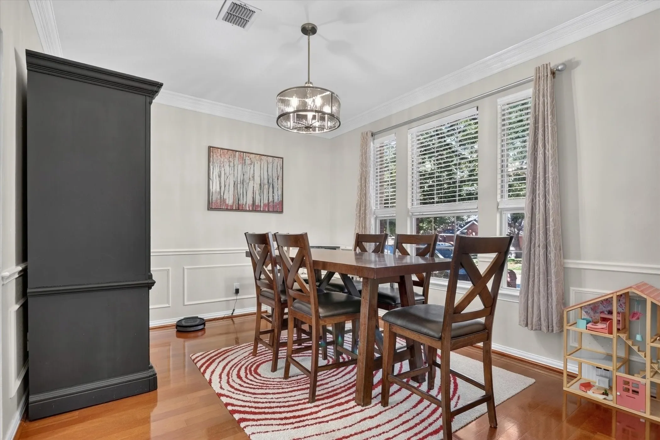 Dining area featuring wood-finish flooring, crown molding, wainscoting, and a multi-light drum chandelier