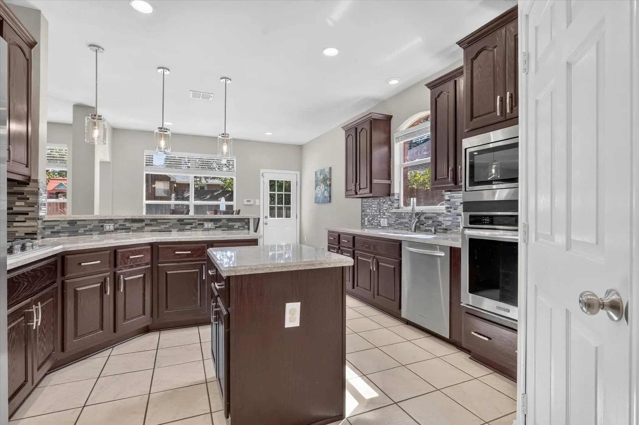 Kitchen featuring dark wood cabinetry, stone-finish countertops, a center island, tile flooring, and stainless steel wall-mounted oven and microwave