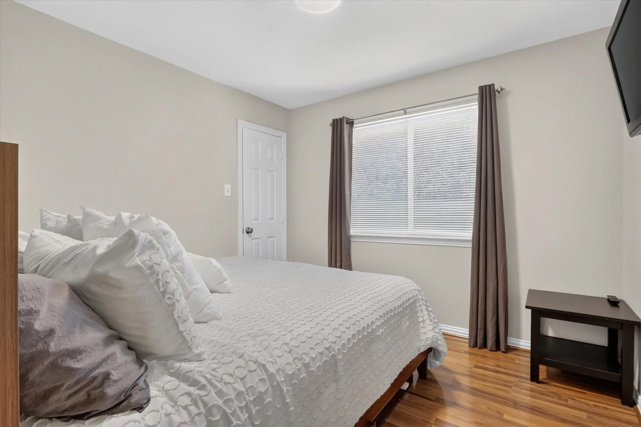 Neutral-toned room with wood-finish flooring, a two-panel interior door, and a horizontal window with integrated blinds