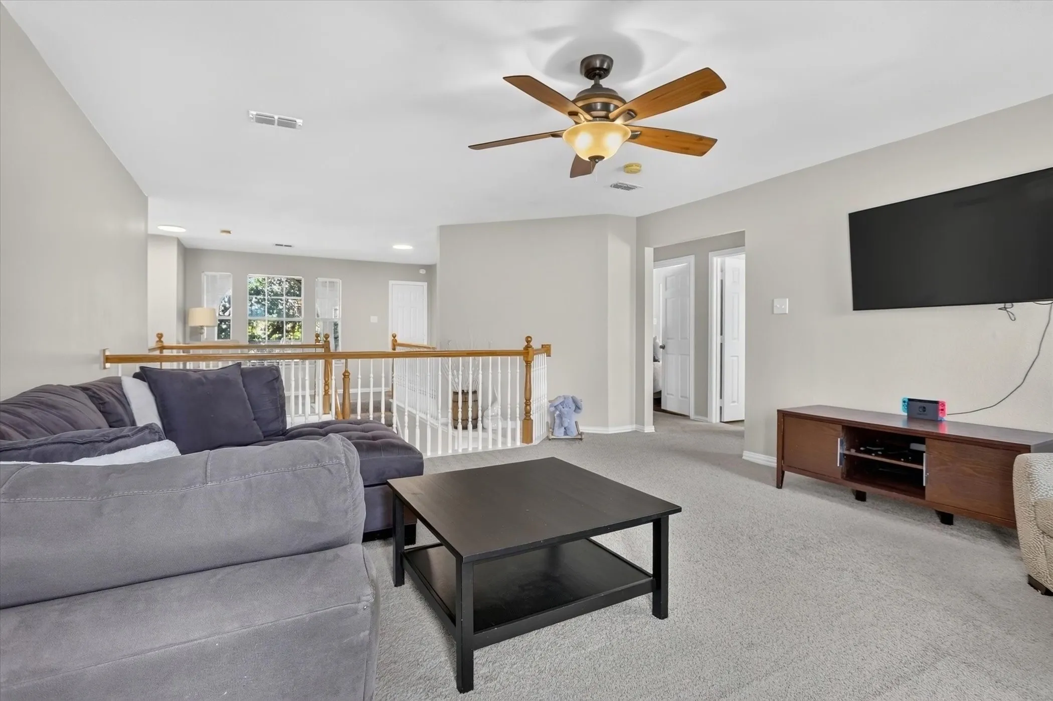 Open interior space featuring a ceiling fan, wall-to-wall carpeting, and a wooden balustrade staircase railing
