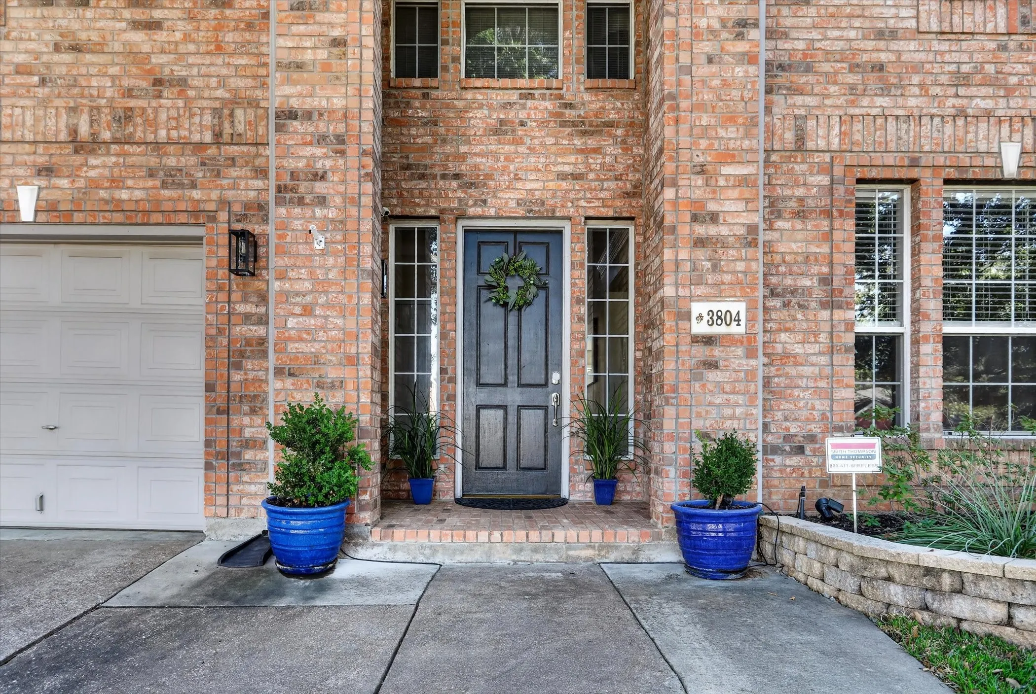 Brick exterior featuring a multi-panel front door, sidelight windows, multi-pane window grids, and a concrete driveway