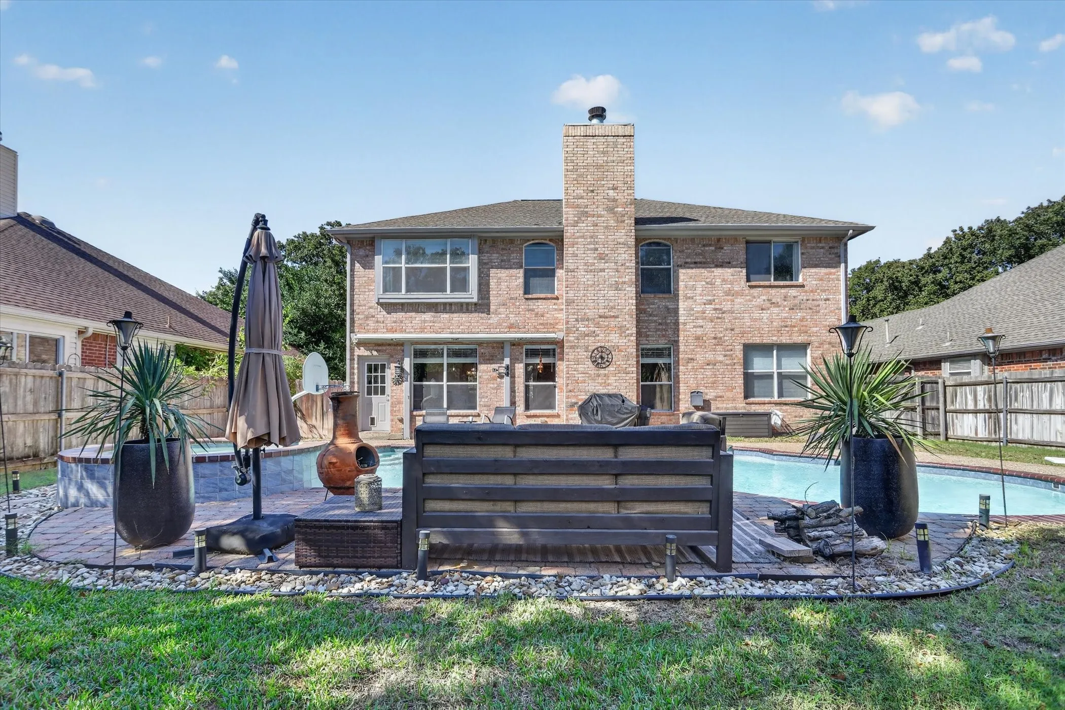 Brick exterior featuring a two-story chimney, inground swimming pool with tiled border, and stone-paver patio