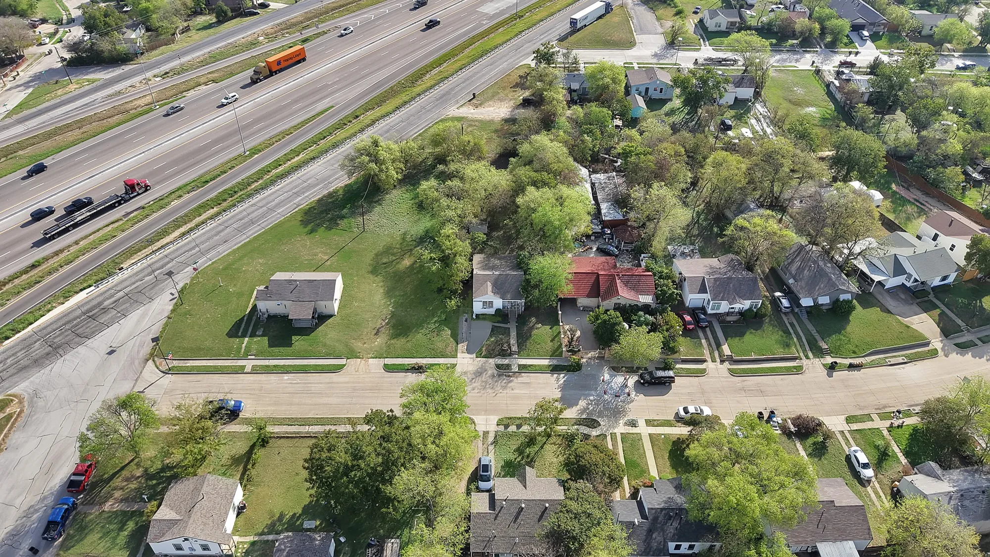Aerial perspective of a residential lot featuring expansive green space, mature trees, and street-front access